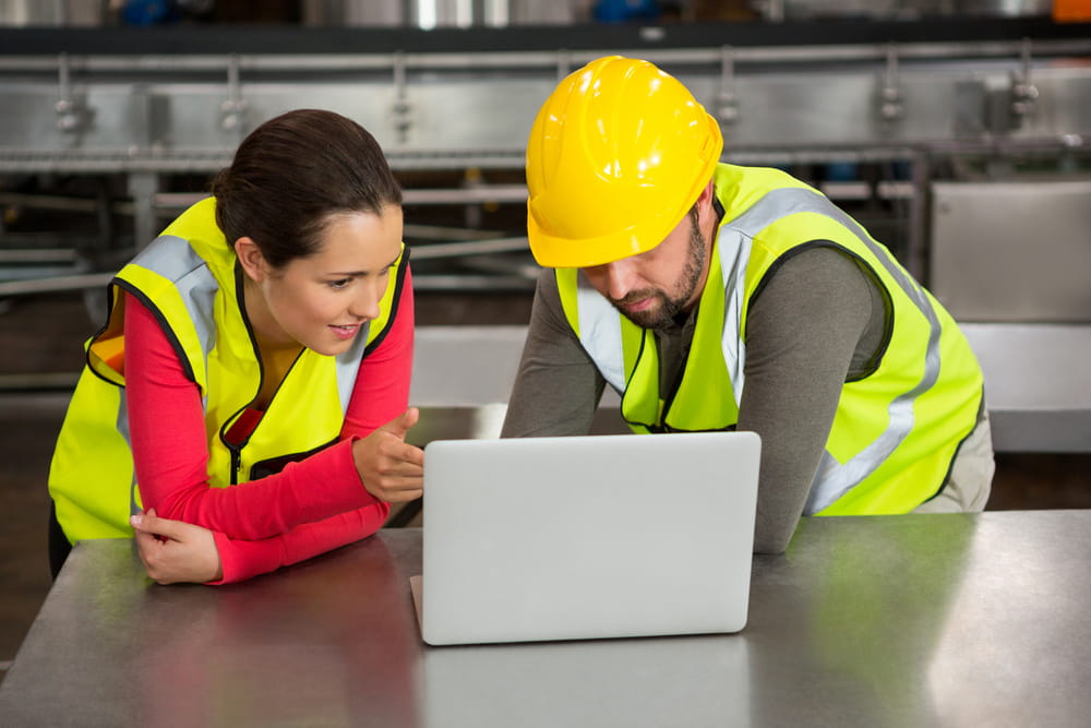 La formazione online sulla sicurezza sul lavoro viene adoperata molto spesso per formare i propri dipendenti. Nella foto, due dipendenti, con casco e giubbotti di sicurezza, che seguono un corso davanti al computer.